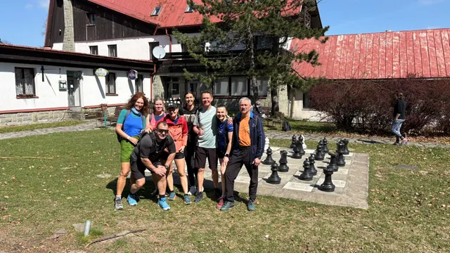 Skupina turistů u horské chaty a velkých venkovních šachů