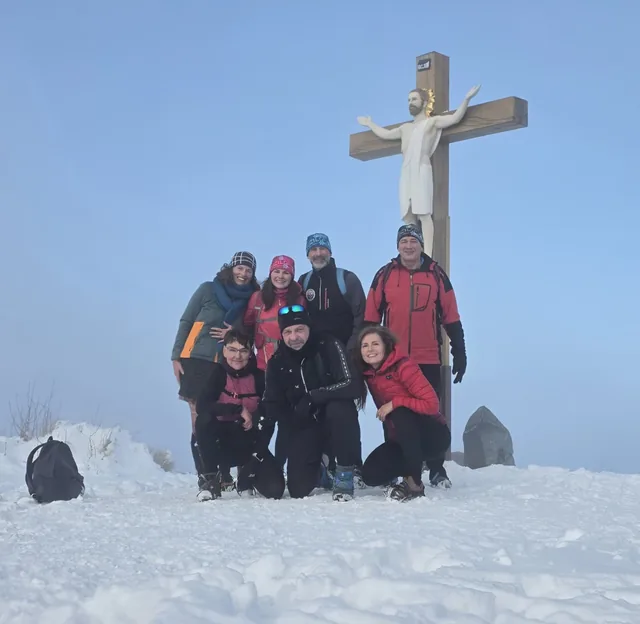 Skupina turistů u kříže na zasněženém vrcholu