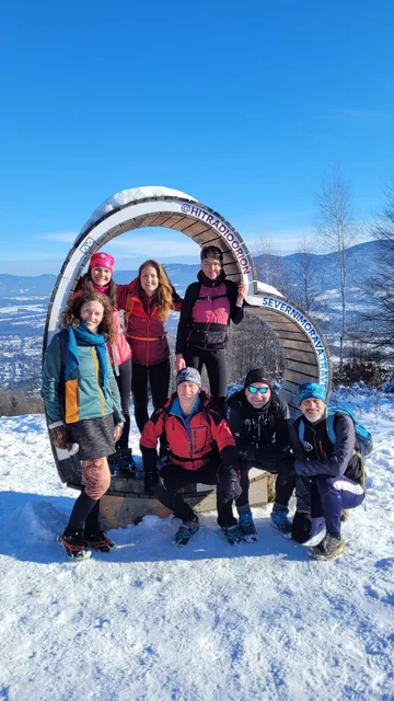 Skupina turistů na zasněženém vrcholu s výhledem na Beskydy